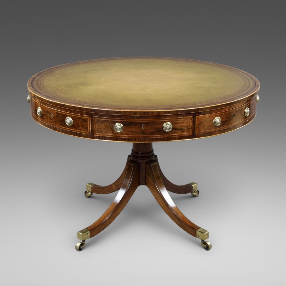 Regency rosewood circular drum table featuring an olive green leather inset top, brass lion-mask drawer handles, and a central pedestal support on splayed quadruped legs with brass castors.