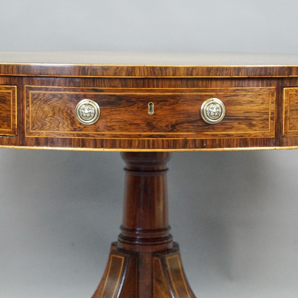 Regency rosewood circular drum table featuring an olive green leather inset top, brass lion-mask drawer handles, and a central pedestal support on splayed quadruped legs with brass castors. View III