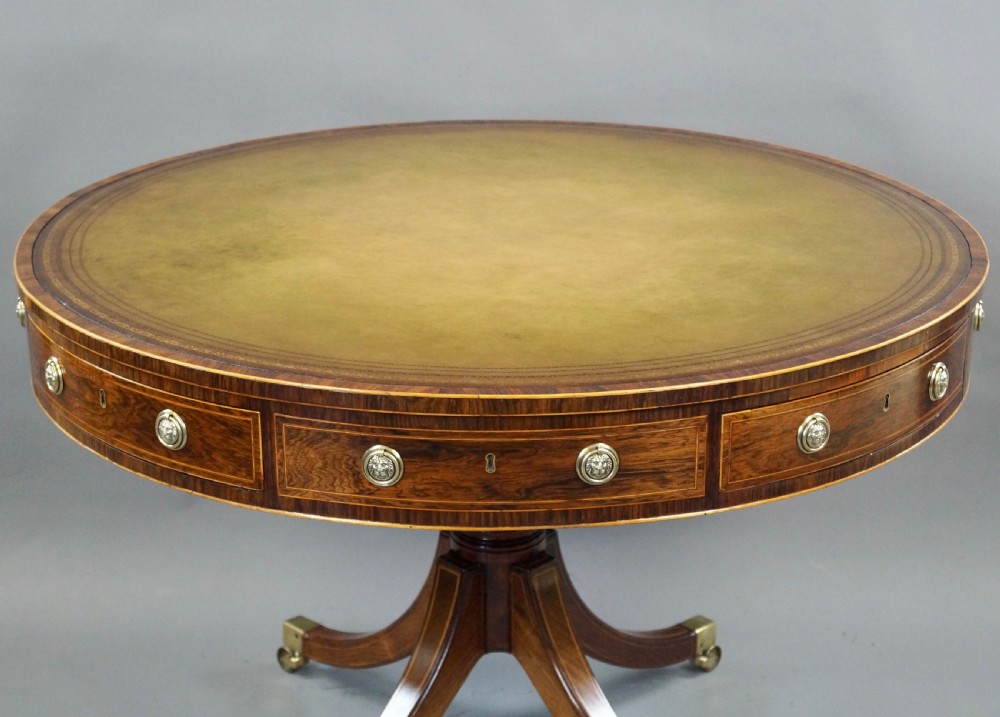 Regency rosewood circular drum table featuring an olive green leather inset top, brass lion-mask drawer handles, and a central pedestal support on splayed quadruped legs with brass castors. View VI
