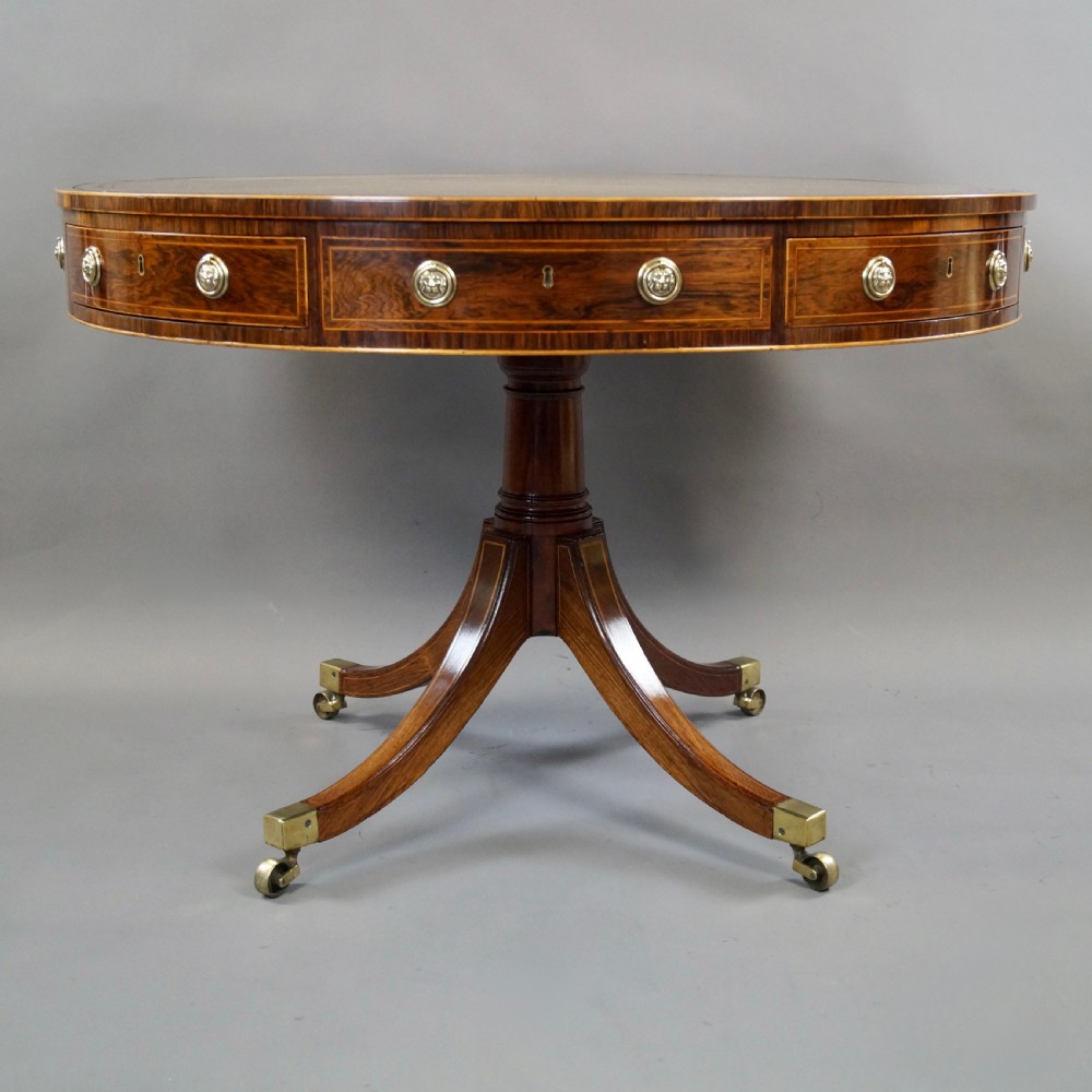 Regency rosewood circular drum table featuring an olive green leather inset top, brass lion-mask drawer handles, and a central pedestal support on splayed quadruped legs with brass castors. View VII