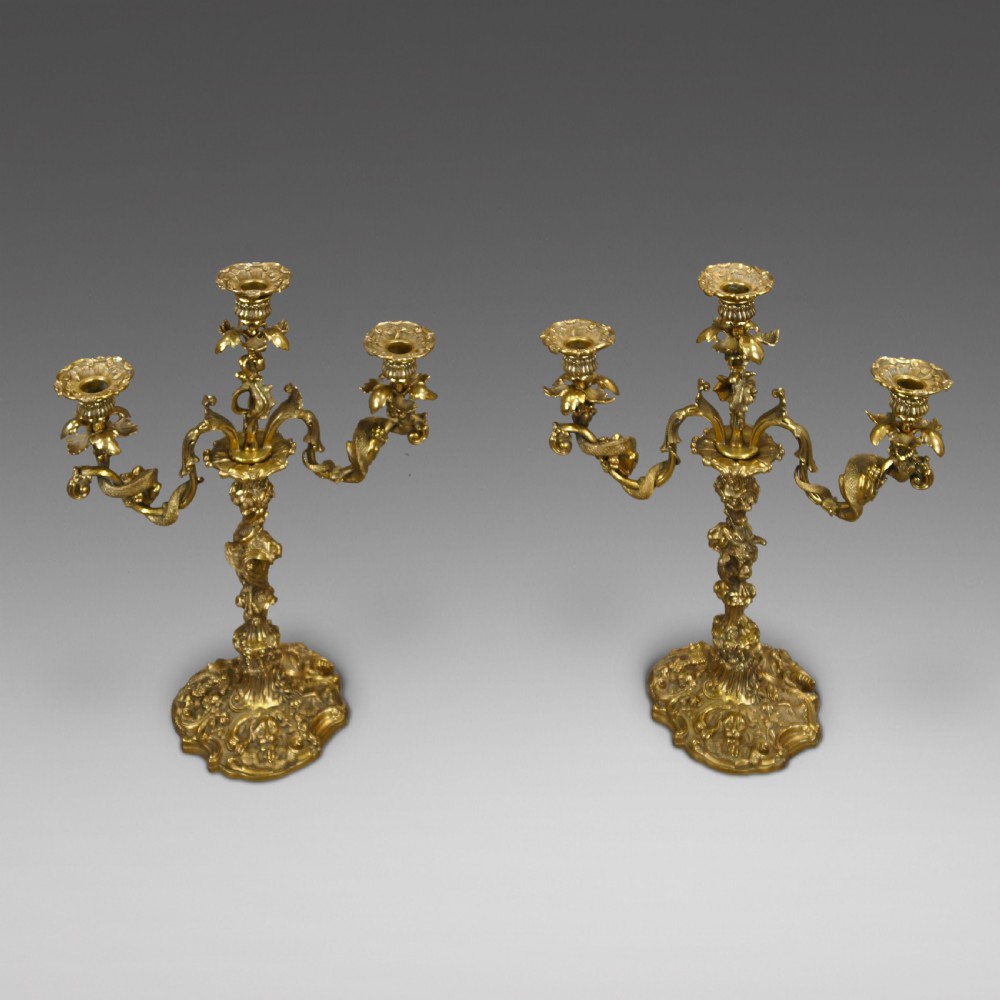 A pair of ornate French Rococo style ormolu three-light candelabra with scrolling leafy arms and intricate cast bases.