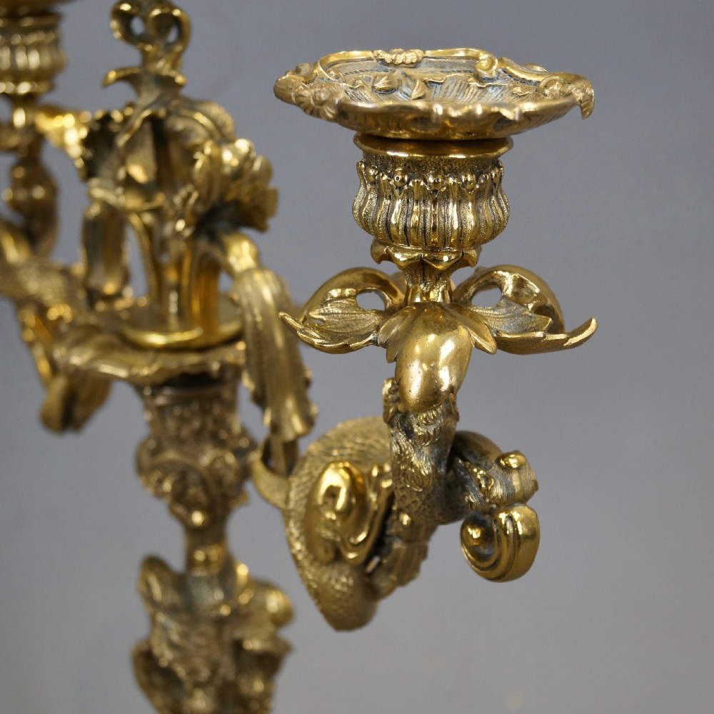 A pair of ornate French Rococo style ormolu three-light candelabra with scrolling leafy arms and intricate cast bases. View V
