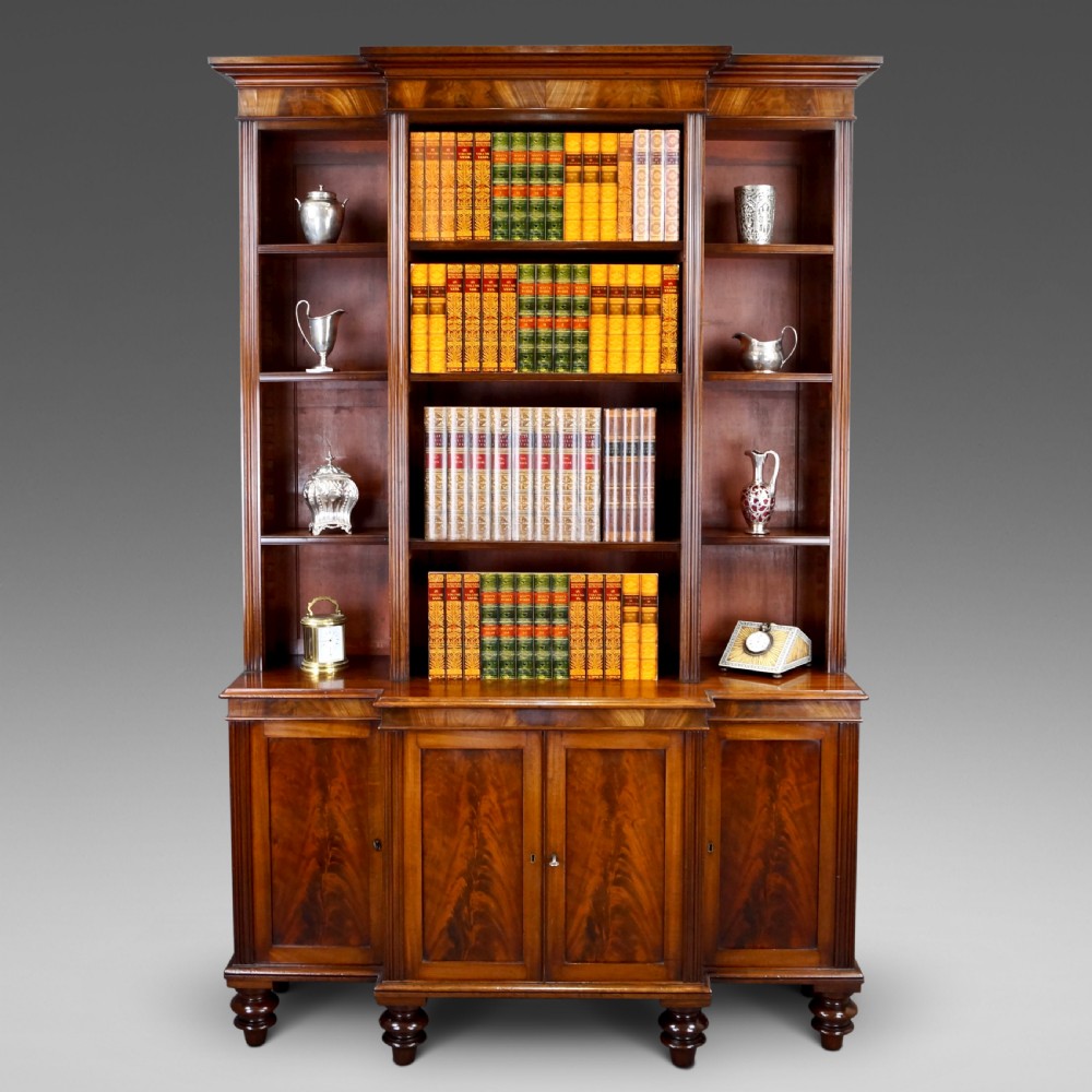 A mahogany breakfront bookcase featuring open upper shelving, flame mahogany panelled lower cupboard doors, and turned feet.