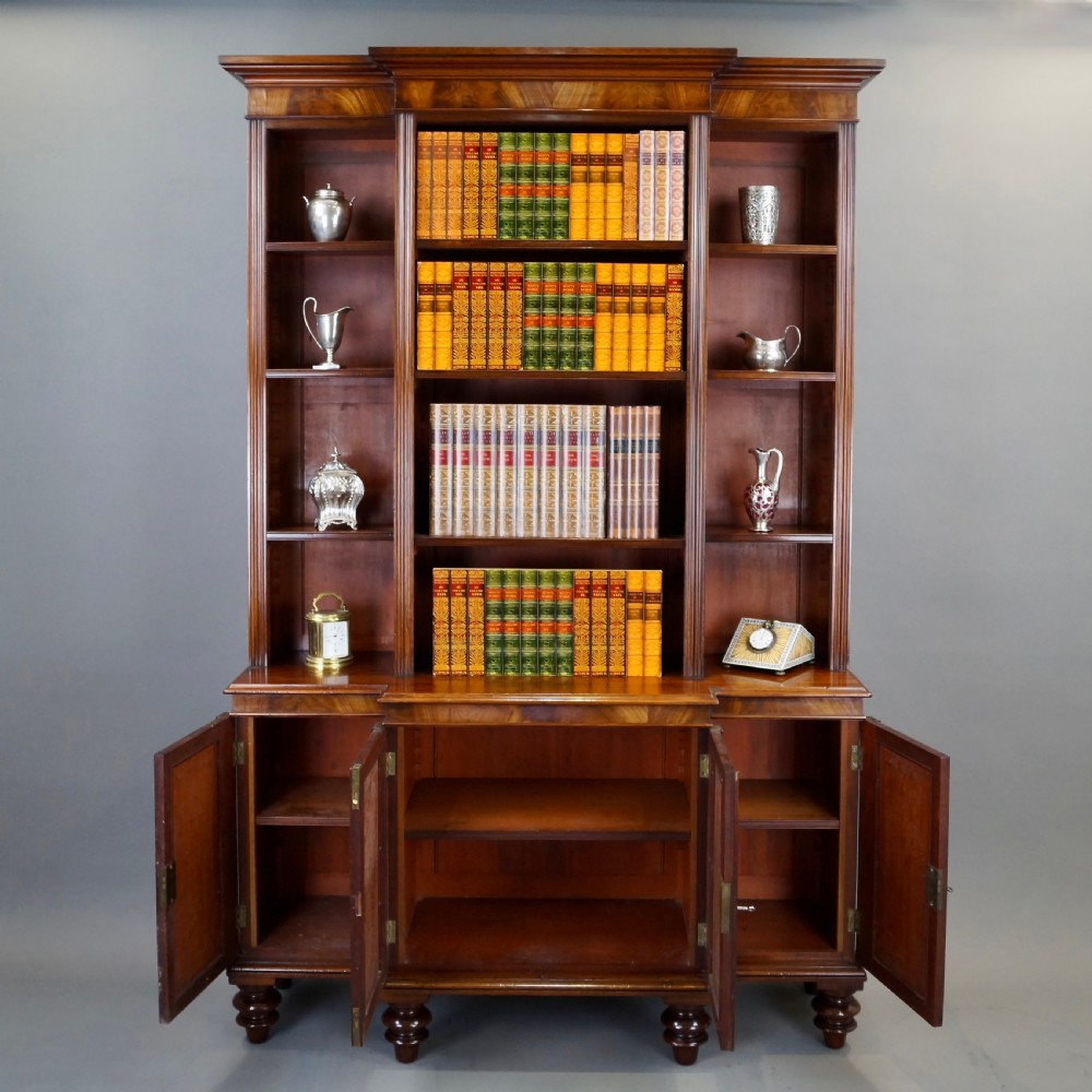 A mahogany breakfront bookcase featuring open upper shelving, flame mahogany panelled lower cupboard doors, and turned feet. View II