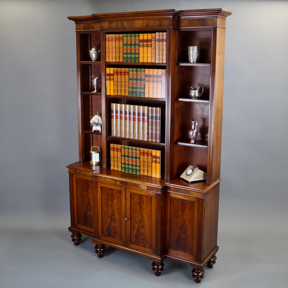 A mahogany breakfront bookcase featuring open upper shelving, flame mahogany panelled lower cupboard doors, and turned feet. View VI