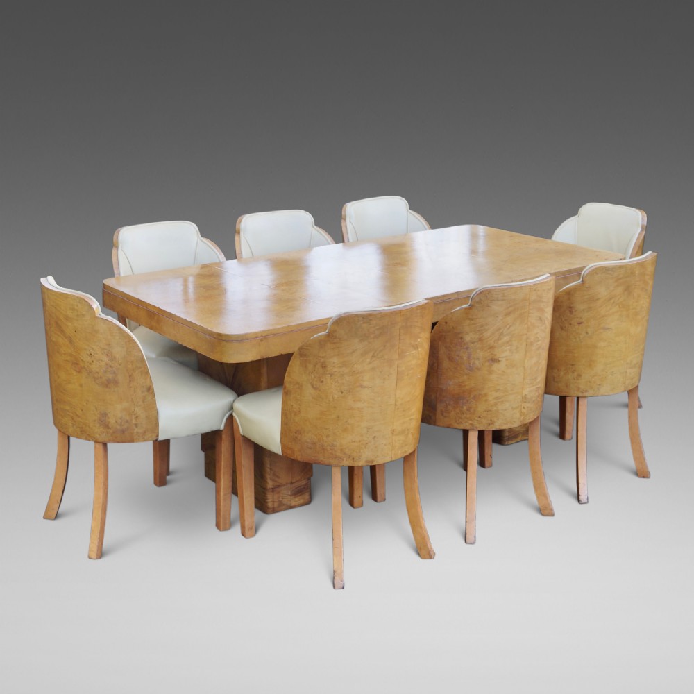 An Art Deco burr walnut dining suite featuring a rectangular pedestal table with curved corners and matching cloud-back chairs upholstered in cream leather.