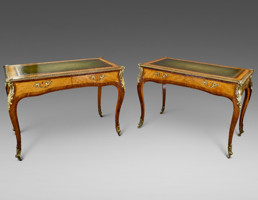 A pair of Louis XV style bureau plat writing desks featuring satinwood marquetry, green leather tops, cabriole legs, and elaborate gilt-bronze mounts.
