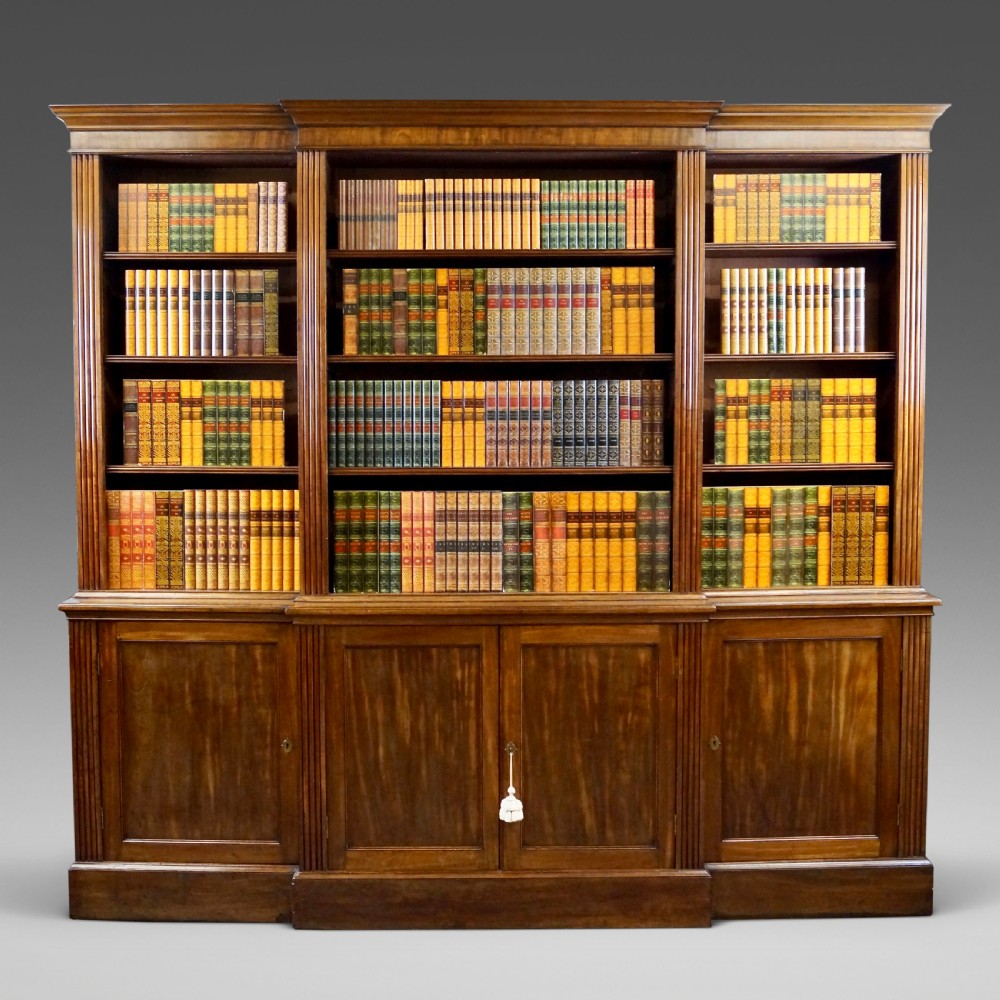 A late George III mahogany breakfront open bookcase featuring fluted pilasters, adjustable upper shelving, and panelled cupboard doors below.