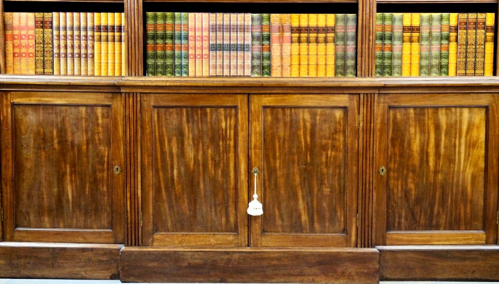A late George III mahogany breakfront open bookcase featuring fluted pilasters, adjustable upper shelving, and panelled cupboard doors below. View III