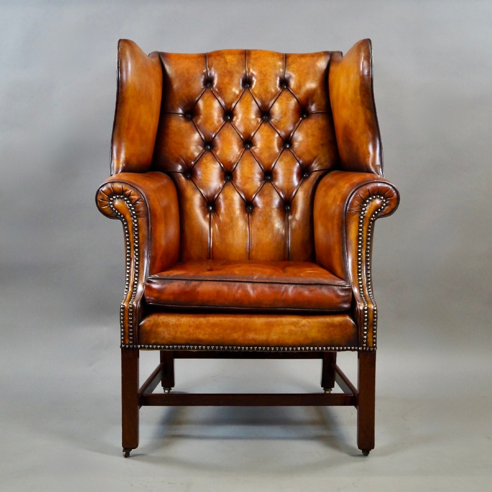 A George III period tan leather wingback armchair featuring deep button tufting, brass stud detailing, scrolled arms, and square mahogany legs united by stretchers. View II