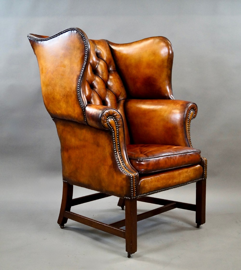 A George III period tan leather wingback armchair featuring deep button tufting, brass stud detailing, scrolled arms, and square mahogany legs united by stretchers. View III