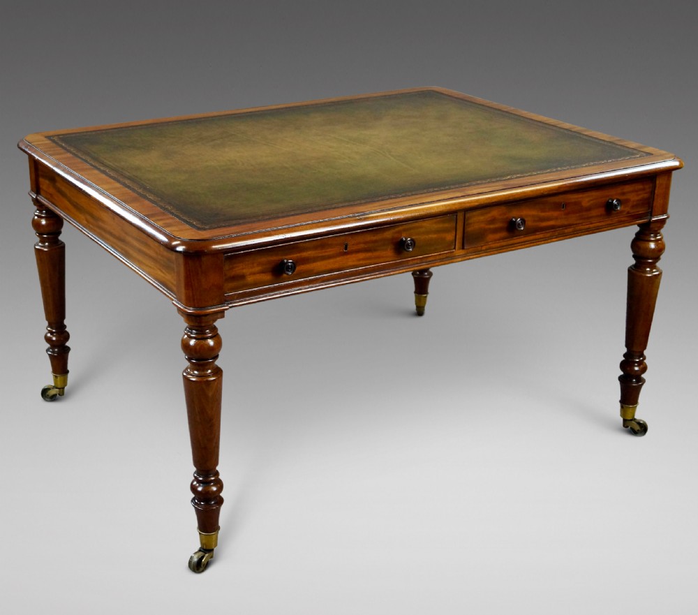 An antique mahogany partners writing table featuring a green leather inset top, two frieze drawers with turned handles, and turned legs on brass castors.
