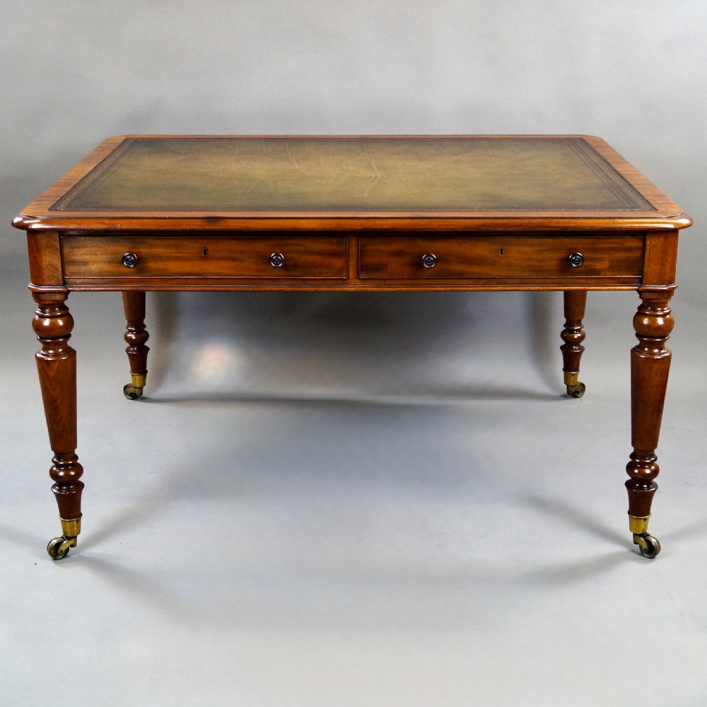 An antique mahogany partners writing table featuring a green leather inset top, two frieze drawers with turned handles, and turned legs on brass castors. View II