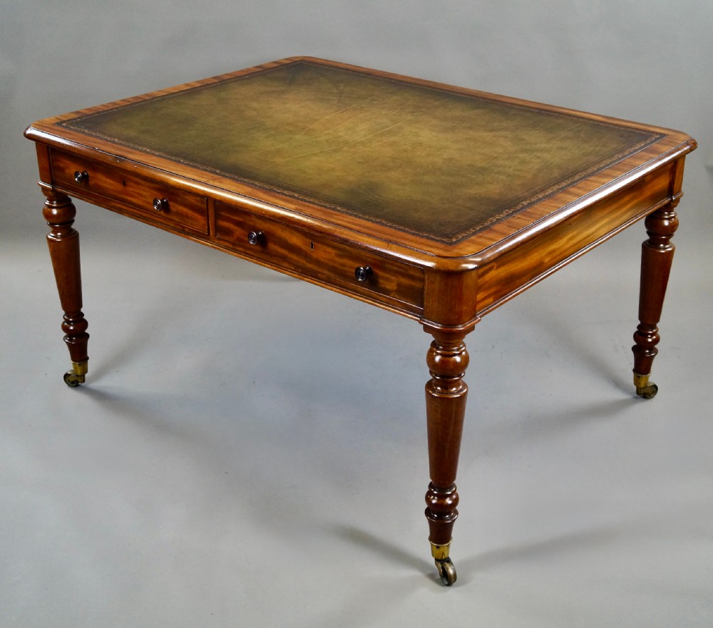 An antique mahogany partners writing table featuring a green leather inset top, two frieze drawers with turned handles, and turned legs on brass castors. View III