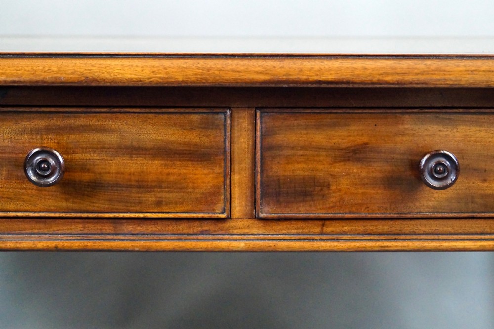 An antique mahogany partners writing table featuring a green leather inset top, two frieze drawers with turned handles, and turned legs on brass castors. View IV