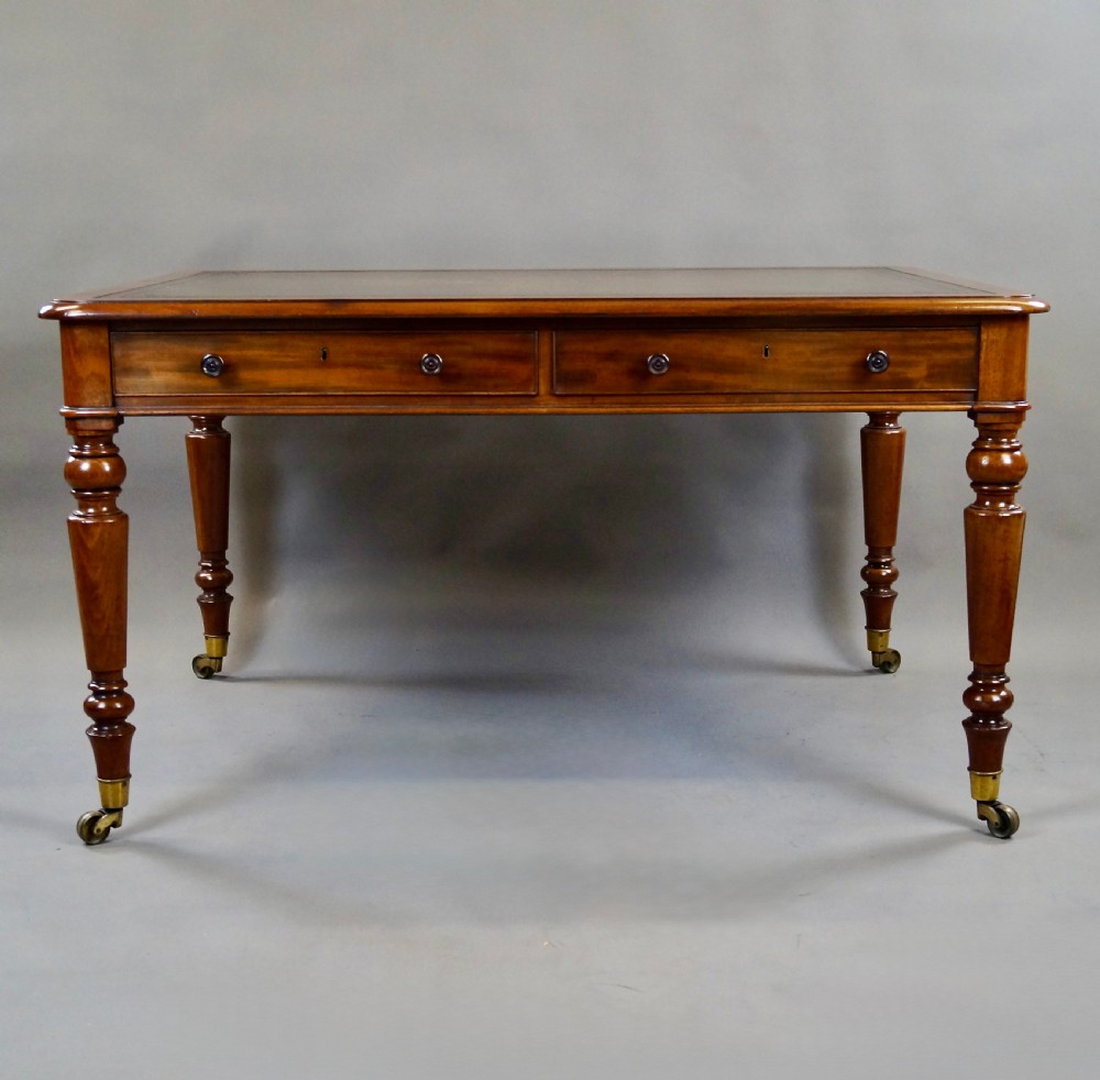 An antique mahogany partners writing table featuring a green leather inset top, two frieze drawers with turned handles, and turned legs on brass castors. View VI