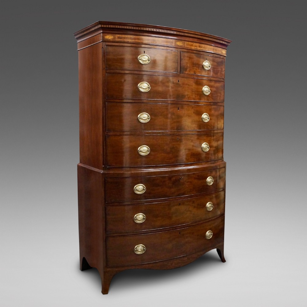 A Georgian mahogany bow-fronted tallboy featuring two sections with multiple graduated drawers, brass oval handles, an inlaid top frieze, and splayed bracket feet.