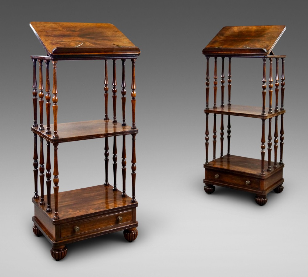 A pair of antique rosewood tiered whatnots featuring adjustable sloped reading tops, turned spindle supports, single drawers at the base, and lobed bun feet.