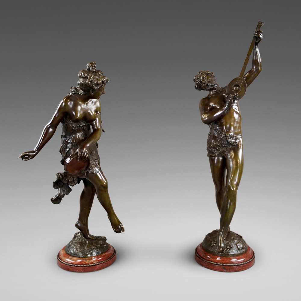 A pair of 19th-century dark bronze sculptures depicting a female musician with a tambourine and a male figure playing a lute, both set on circular red marble bases.