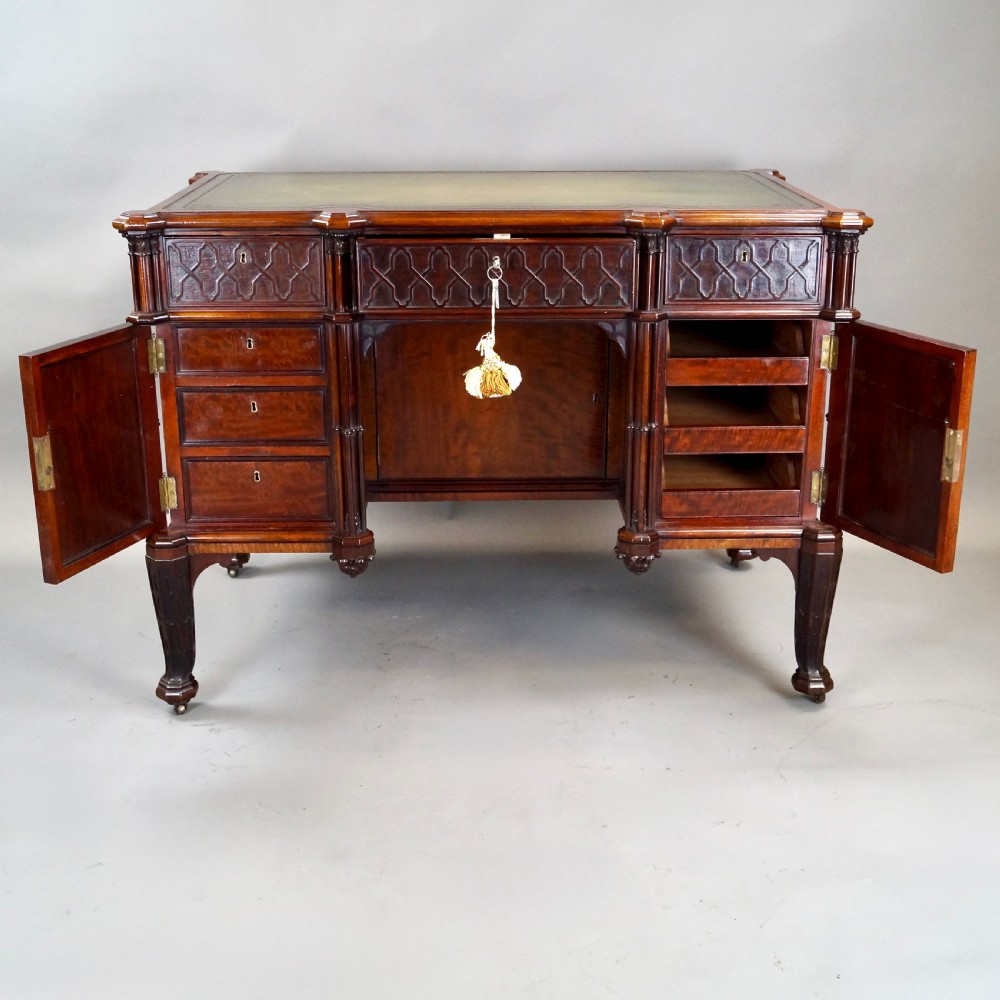 A Chippendale style dark mahogany Gothic Revival kneehole desk featuring carved tracery cupboard doors, a green leather writing surface, and carved legs. View IV