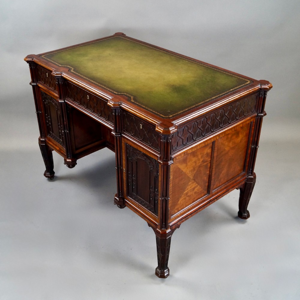 A Chippendale style dark mahogany Gothic Revival kneehole desk featuring carved tracery cupboard doors, a green leather writing surface, and carved legs. View VI