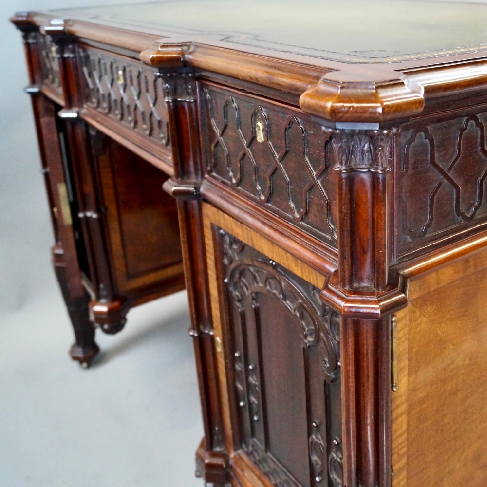A Chippendale style dark mahogany Gothic Revival kneehole desk featuring carved tracery cupboard doors, a green leather writing surface, and carved legs. View VIII
