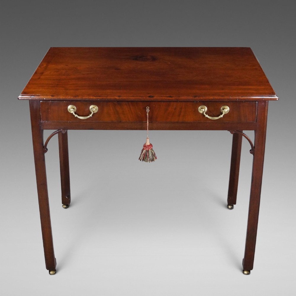 A George III mahogany side table featuring a rectangular top, single frieze drawer with brass swan-neck handles, corner brackets, and square legs on brass castors.