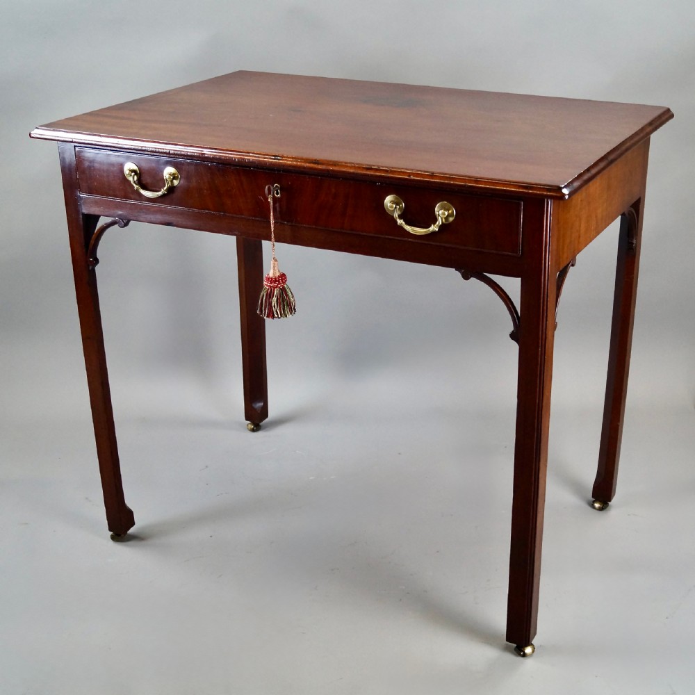 A George III mahogany side table featuring a rectangular top, single frieze drawer with brass swan-neck handles, corner brackets, and square legs on brass castors. View II