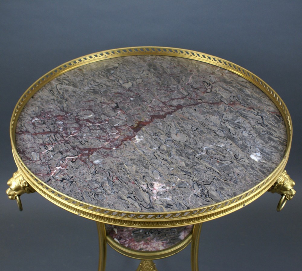 A circular French ormolu gueridon table featuring grey marble tops, a pierced gilt gallery, lion mask mounts with ring handles, and tripod legs terminating in paw feet. View III