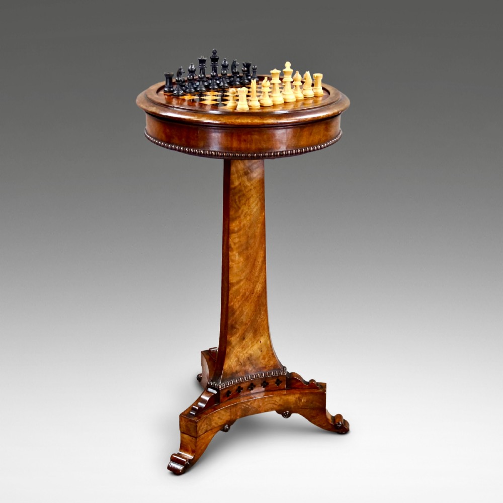 A William IV mahogany circular chess table with an inlaid board, tapered central stem, and triform base on scroll feet.