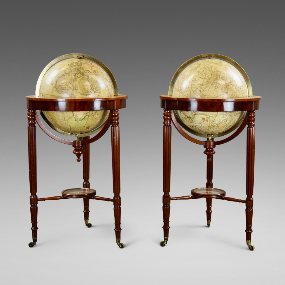 A pair of floor-standing antique globes on turned mahogany reeded legs with brass meridian rings and integral compasses set into the lower stretchers.
