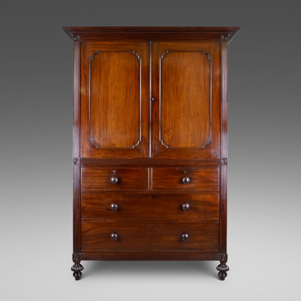 A Regency Cuban mahogany linen press featuring a two-door upper cupboard with panelled doors flanked by reeded pilasters over a lower chest of drawers raised on turned feet.