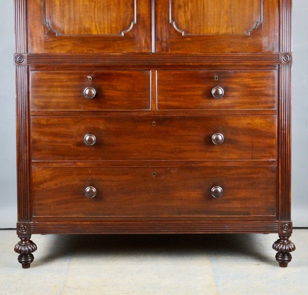 A Regency Cuban mahogany linen press featuring a two-door upper cupboard with panelled doors flanked by reeded pilasters over a lower chest of drawers raised on turned feet. View III
