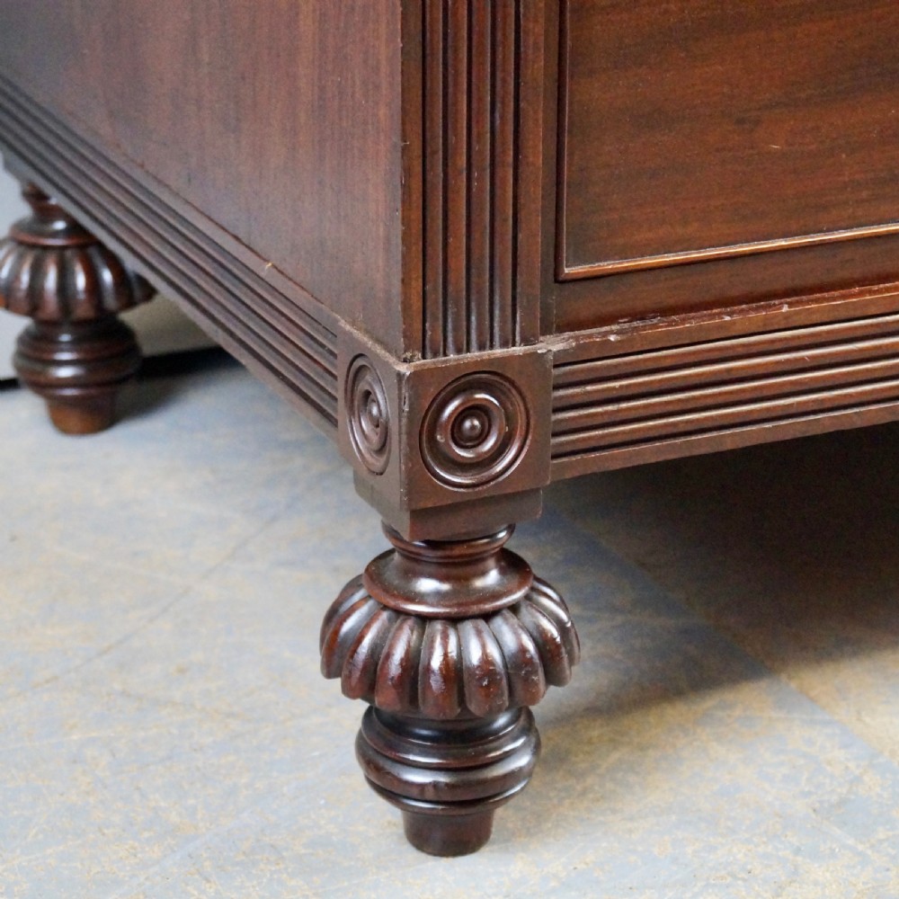 A Regency Cuban mahogany linen press featuring a two-door upper cupboard with panelled doors flanked by reeded pilasters over a lower chest of drawers raised on turned feet. View IV