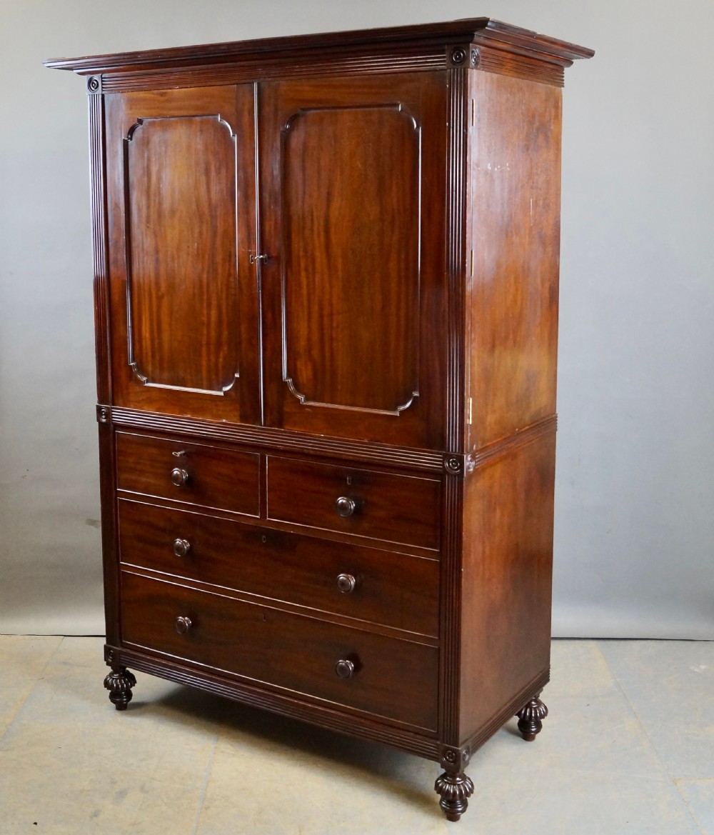 A Regency Cuban mahogany linen press featuring a two-door upper cupboard with panelled doors flanked by reeded pilasters over a lower chest of drawers raised on turned feet. View VI