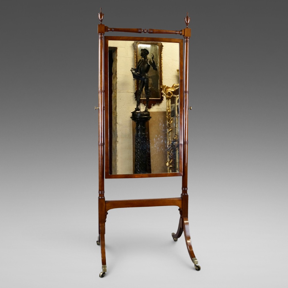 A George III mahogany cheval mirror featuring an adjustable rectangular glass plate suspended between turned vertical supports topped with urn finials and resting on splayed legs with brass castors.