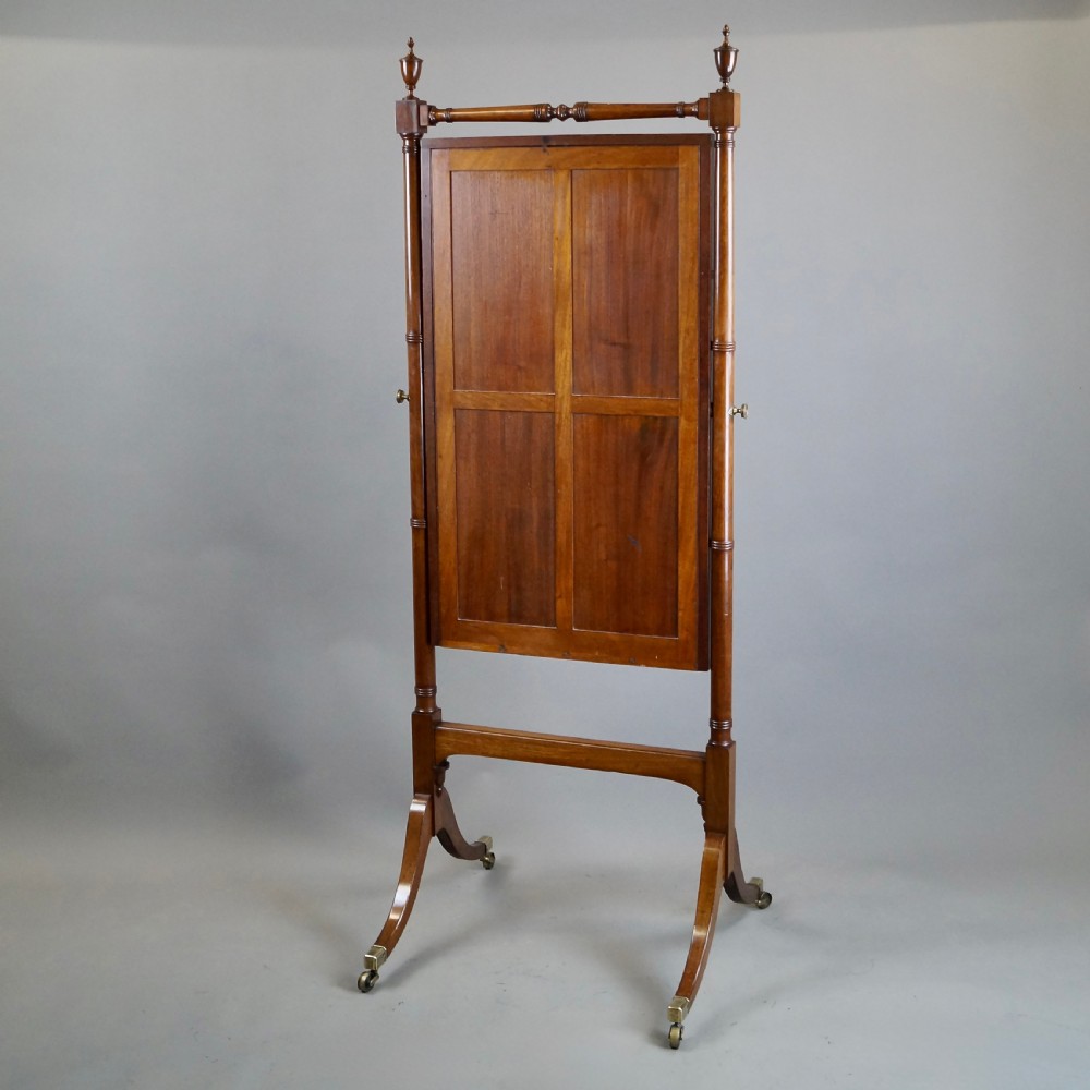 A George III mahogany cheval mirror featuring an adjustable rectangular glass plate suspended between turned vertical supports topped with urn finials and resting on splayed legs with brass castors. View VI
