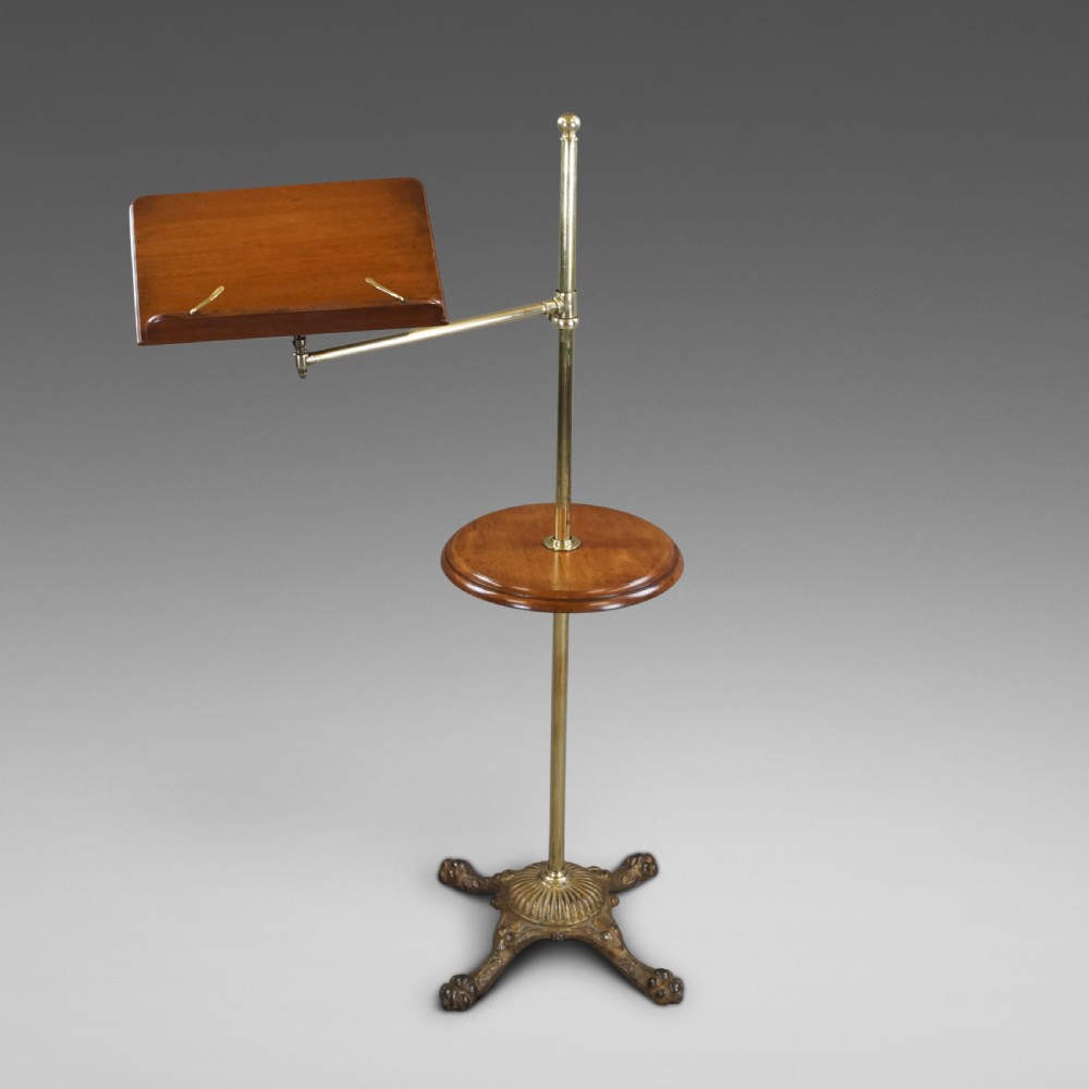 A late 19th-century Victorian reading stand with an adjustable brass stem, articulated arm holding a tilted mahogany book rest, a small central round mahogany shelf, and an ornate cast base. View V