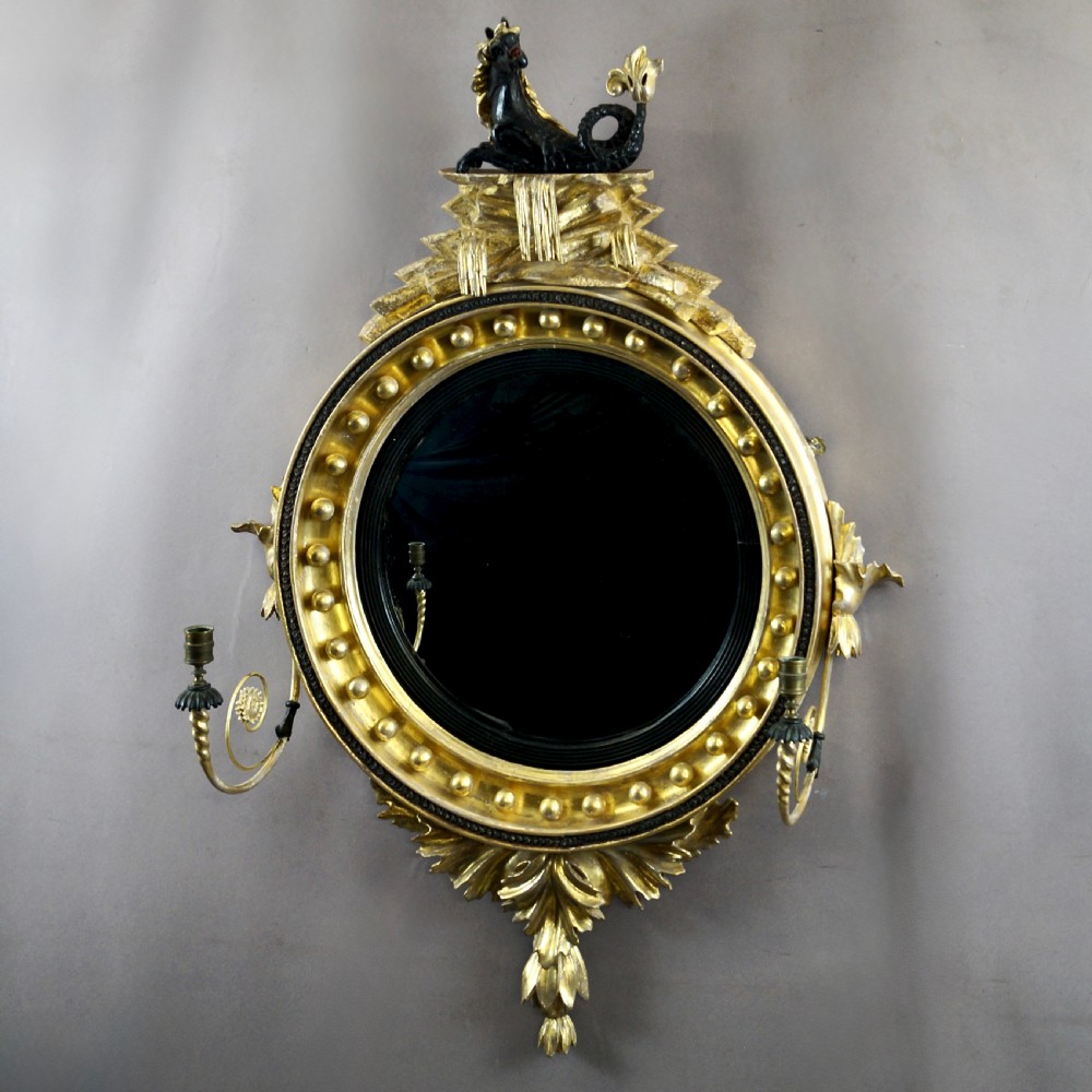 A circular Regency convex giltwood mirror with spherule embellishments, an ebonised dragon cresting, acanthus leaf apron, and twin candle sconces. View III