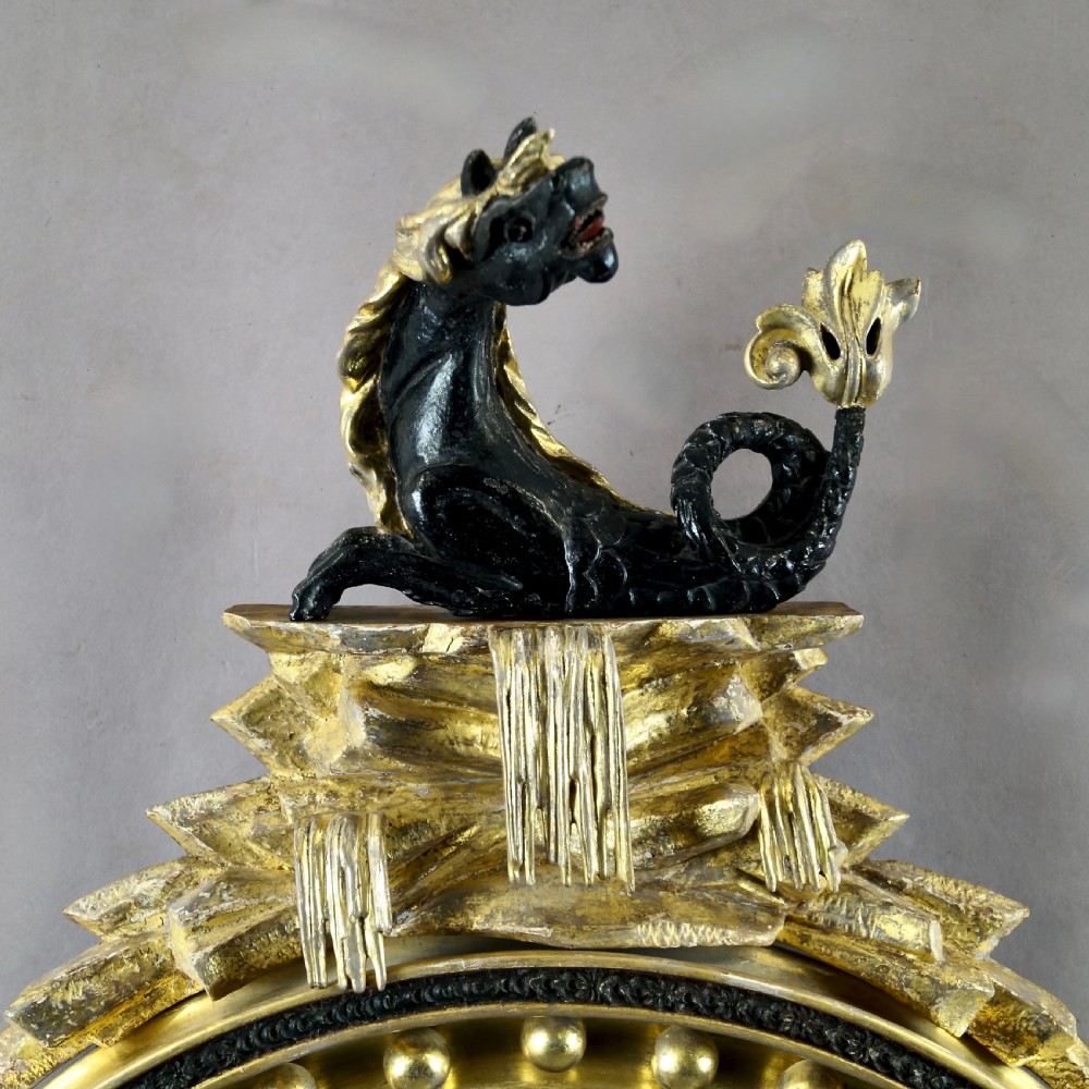 A circular Regency convex giltwood mirror with spherule embellishments, an ebonised dragon cresting, acanthus leaf apron, and twin candle sconces. View IV