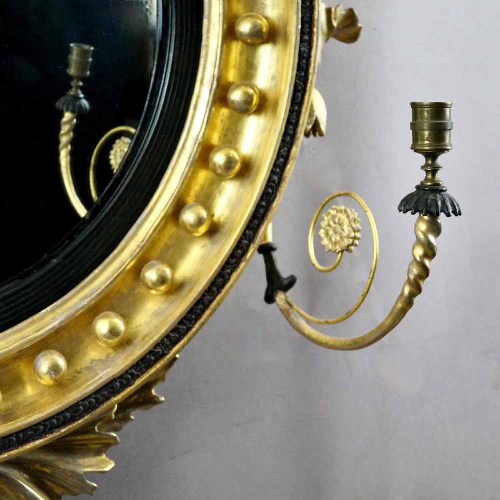 A circular Regency convex giltwood mirror with spherule embellishments, an ebonised dragon cresting, acanthus leaf apron, and twin candle sconces. View V