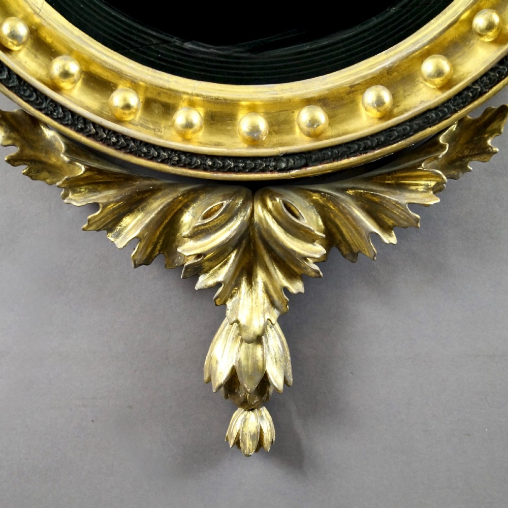 A circular Regency convex giltwood mirror with spherule embellishments, an ebonised dragon cresting, acanthus leaf apron, and twin candle sconces. View VI