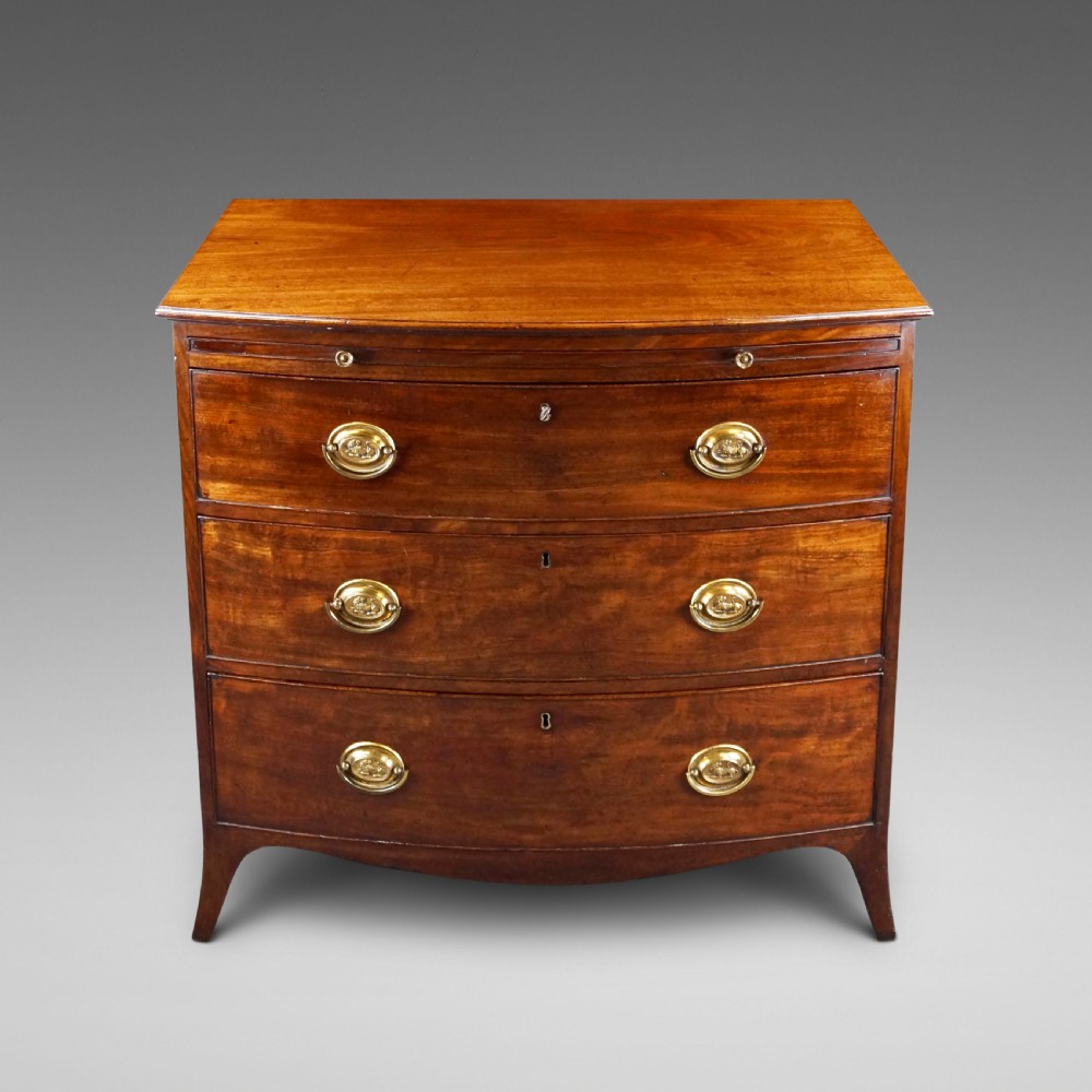A George III mahogany bow-fronted chest of drawers featuring three graduated drawers with brass oval handles, a upper brushing slide, and splayed bracket feet.