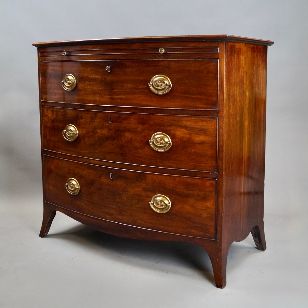 A George III mahogany bow-fronted chest of drawers featuring three graduated drawers with brass oval handles, a upper brushing slide, and splayed bracket feet. View V