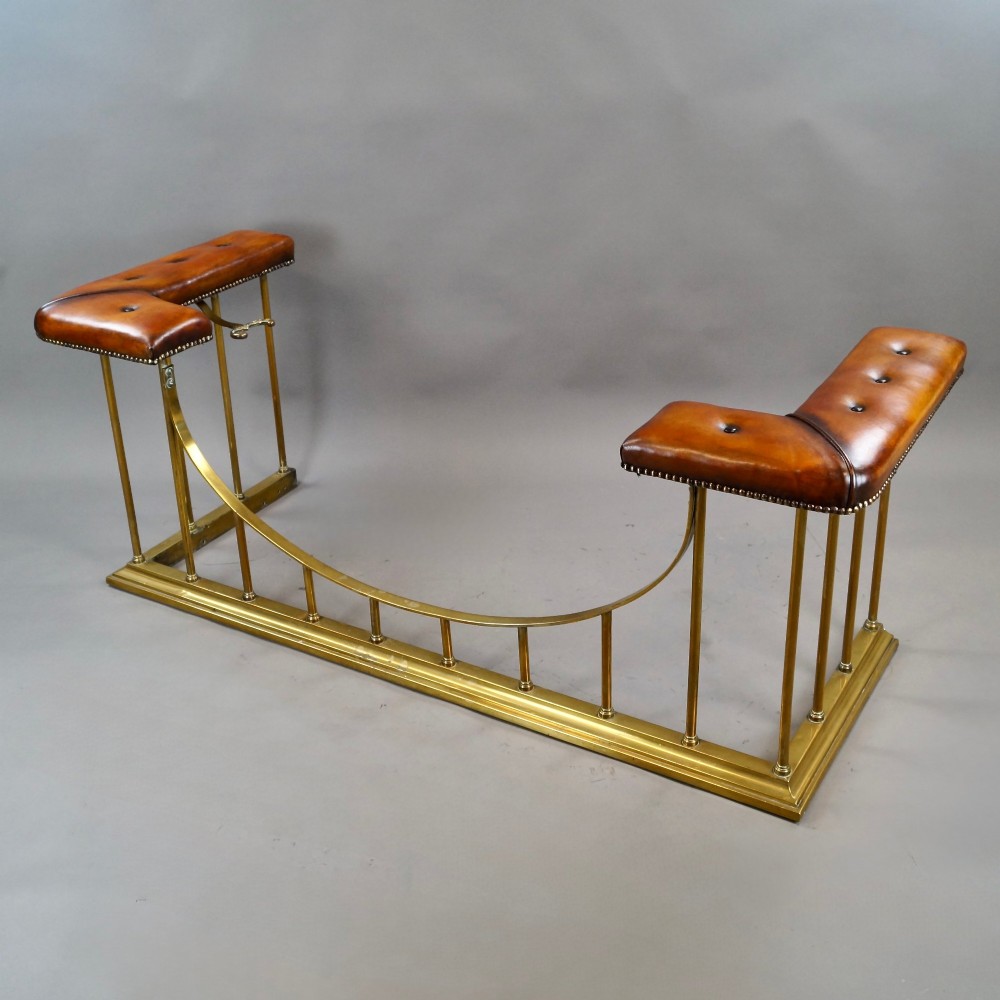 A nineteenth-century brass club fender featuring a central dipped rail, vertical brass spindles, and button-tufted tan leather corner seats. View II