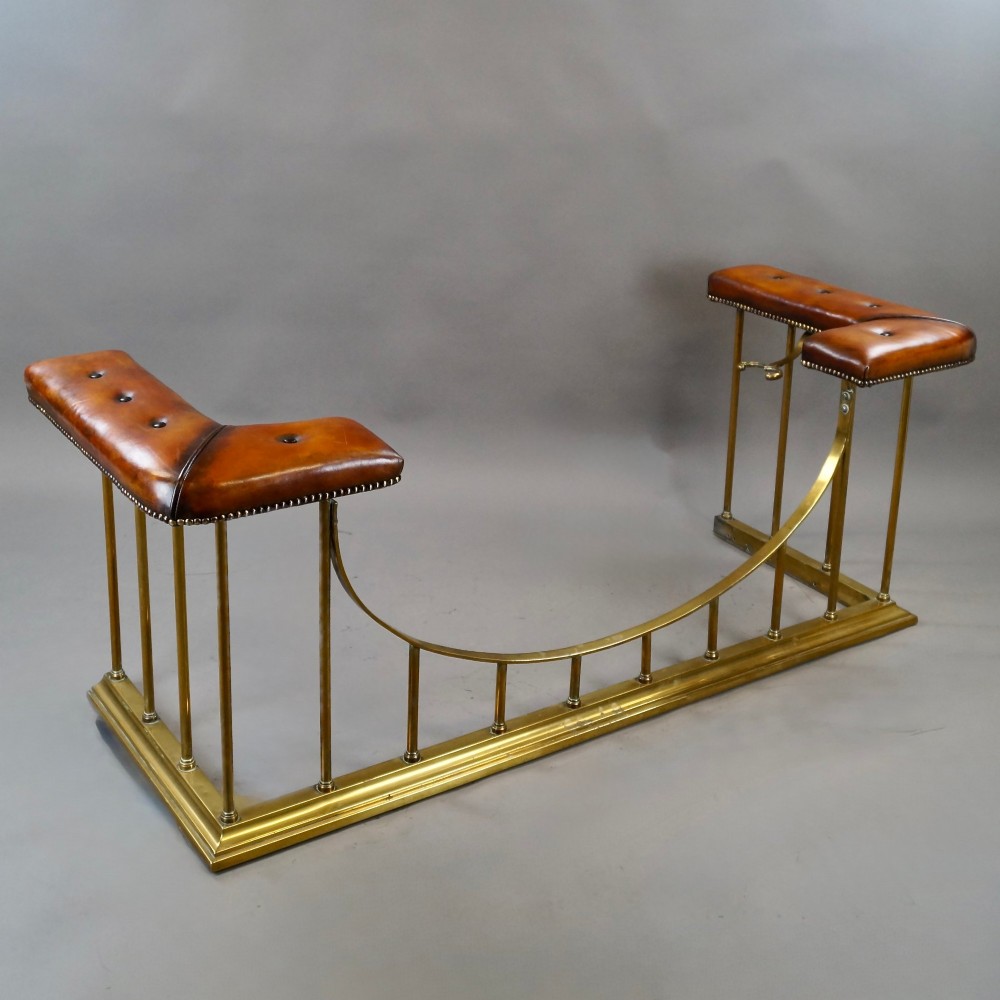 A nineteenth-century brass club fender featuring a central dipped rail, vertical brass spindles, and button-tufted tan leather corner seats. View IV