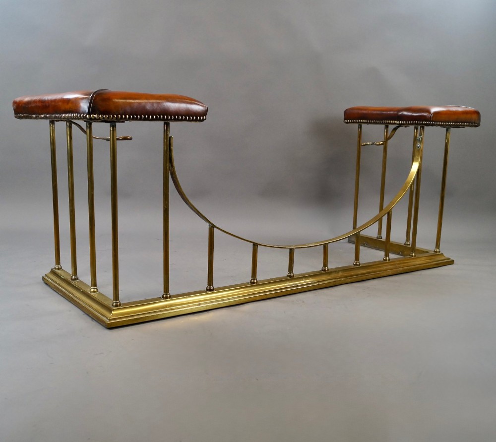 A nineteenth-century brass club fender featuring a central dipped rail, vertical brass spindles, and button-tufted tan leather corner seats. View VI