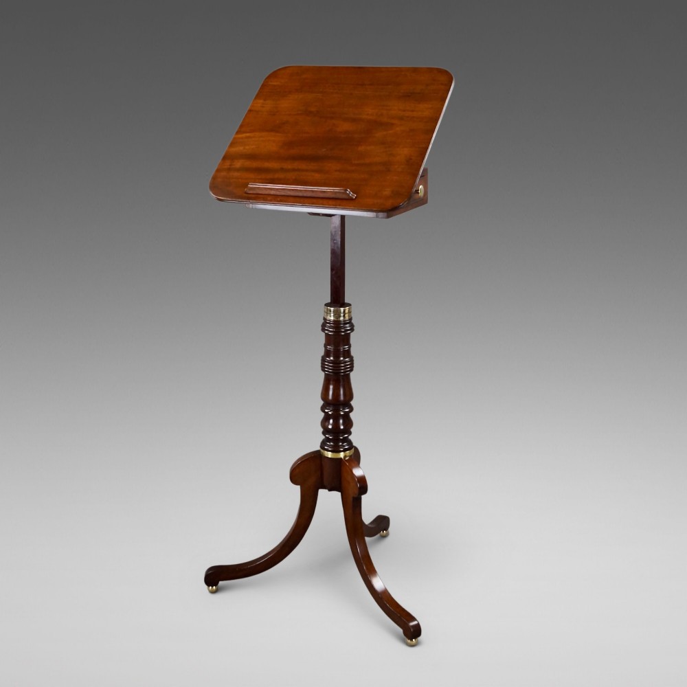 An antique Regency mahogany reading stand featuring an adjustable tilting book rest, turned central stem, brass accents, and sweeping tripod legs.