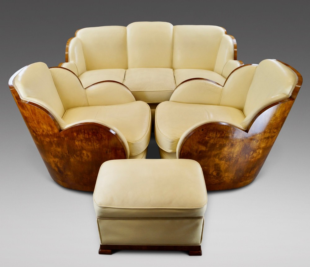 An Art Deco cloud-back lounge suite comprising a three-seater sofa, two matching armchairs, and an ottoman, all upholstered in cream leather with dark burr walnut bentwood outer panels. View II