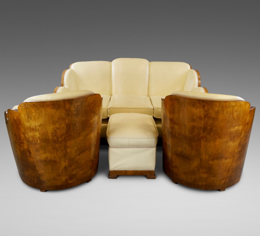 An Art Deco cloud-back lounge suite comprising a three-seater sofa, two matching armchairs, and an ottoman, all upholstered in cream leather with dark burr walnut bentwood outer panels. View III